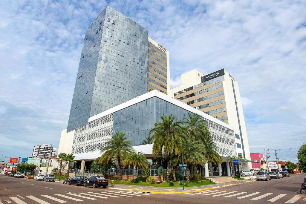 a tall building with palm trees in front of a street at Slaviero Rondonópolis in Rondonópolis