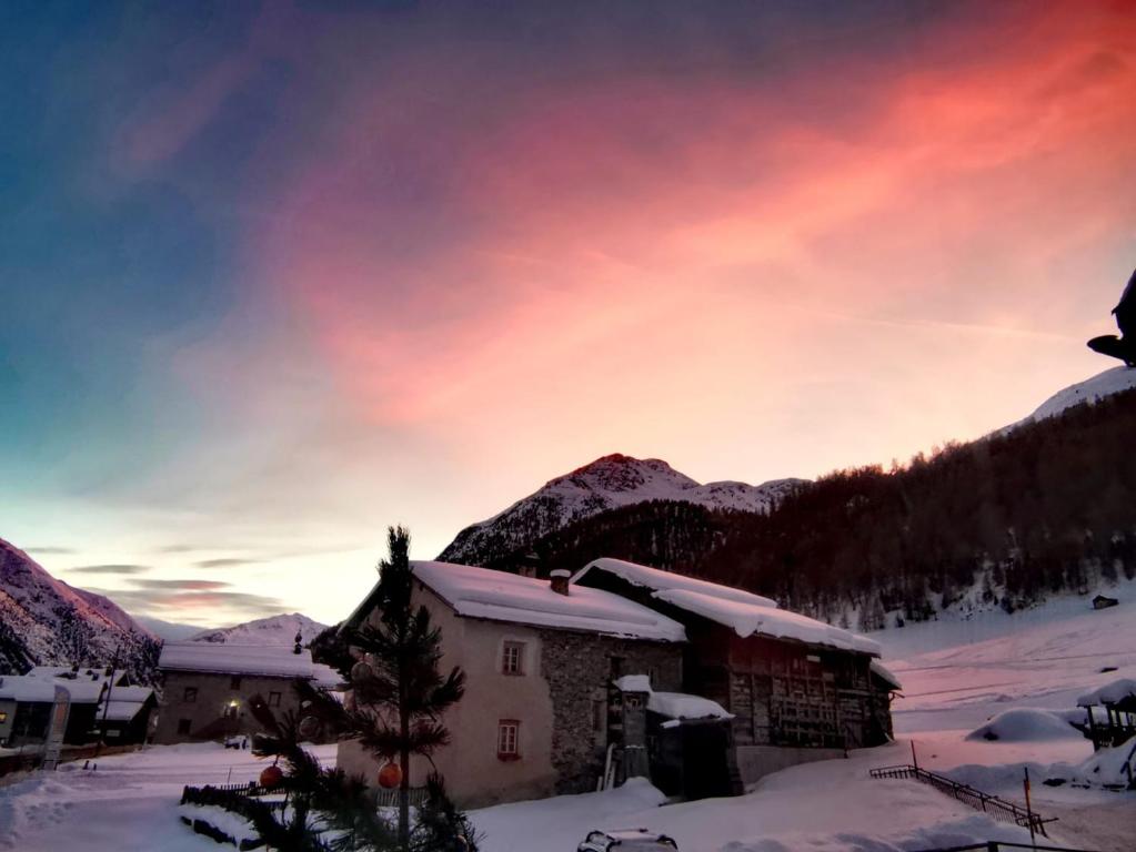 uma casa na neve com um pôr-do-sol ao fundo em Baita Bruno Fior di Loto em Livigno