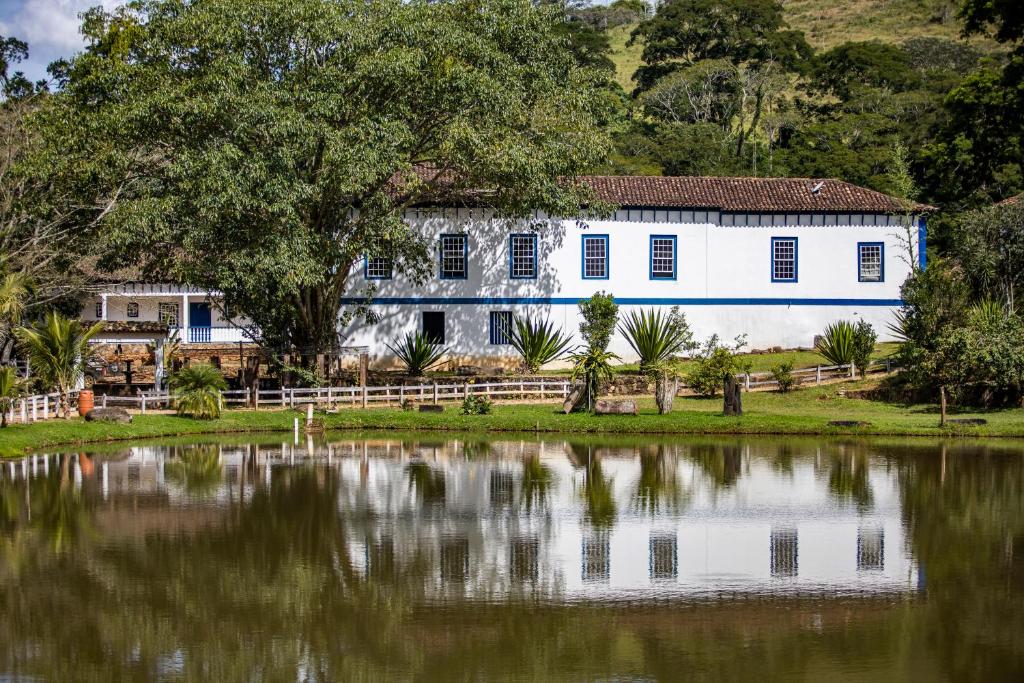 a white house next to a body of water at HOTEL FAZENDA PACIENCIA in Santana dos Montes