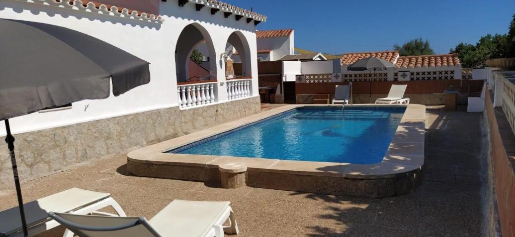 a swimming pool with chairs and an umbrella next to a house at Villa Martínez in Cala en Porter