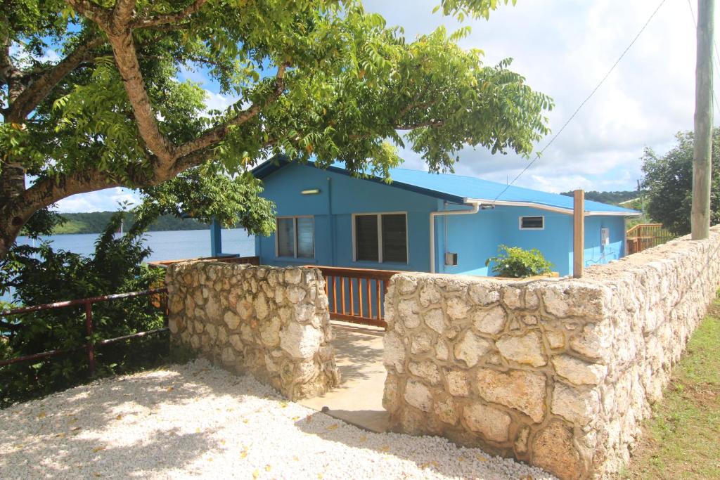 a blue house with a stone wall in front of it at Boathouse Apartments in Neiafu