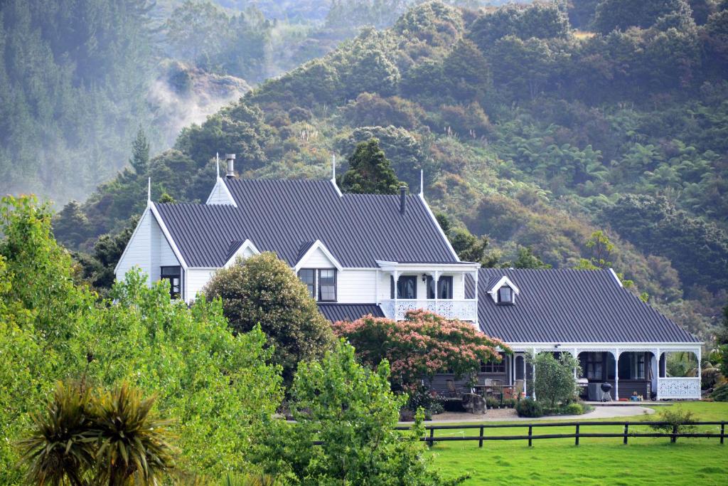 Une grande maison blanche avec une montagne en arrière-plan dans l'établissement Country Homestead at Black Sheep Farm, à Waipu