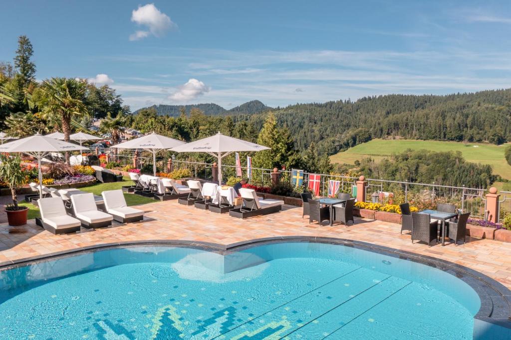 a swimming pool with chairs and umbrellas on a resort at Hotel Dollenberg in Bad Peterstal-Griesbach