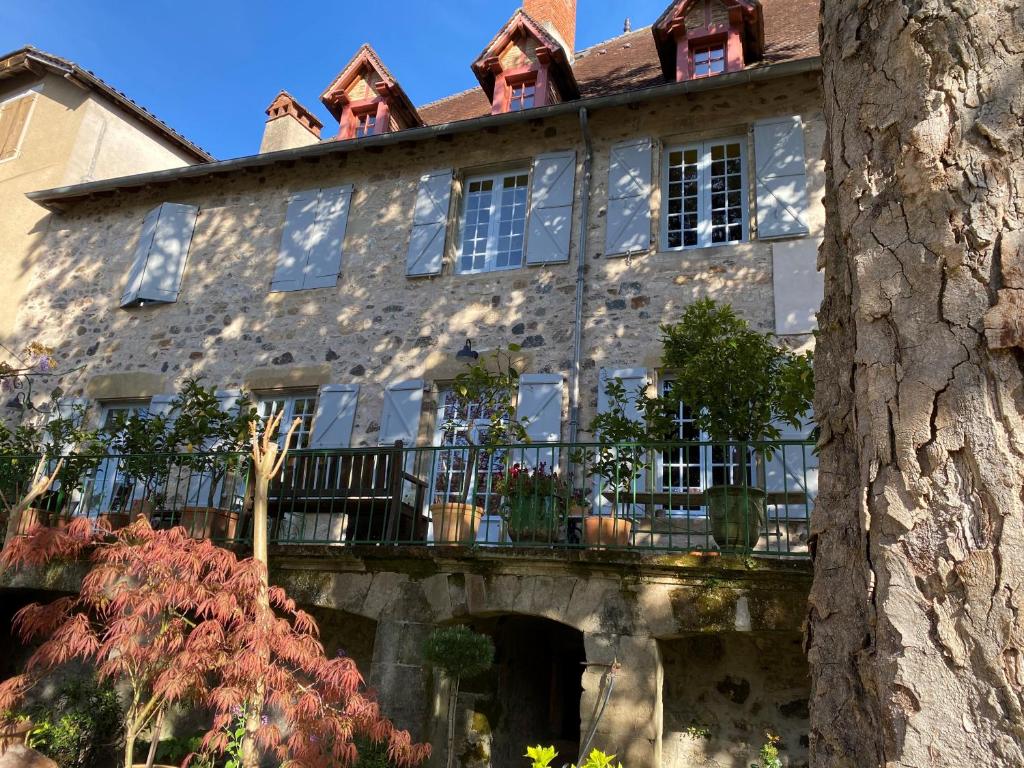 an old stone house with a balcony and a tree at Le Clos Rodolphe in Beaulieu-sur-Dordogne