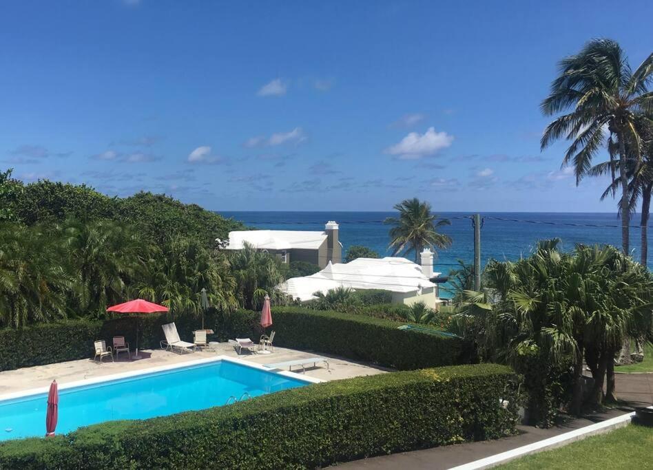 a swimming pool with the ocean in the background at Bermuda At the Beach One-Bedroom in Paget Parish