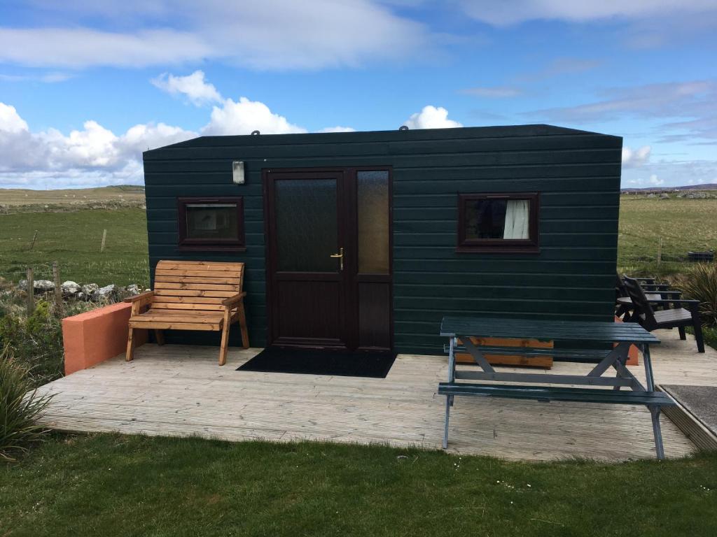 a green tiny house with a bench and a table at Dallymach pod in Lochboisdale