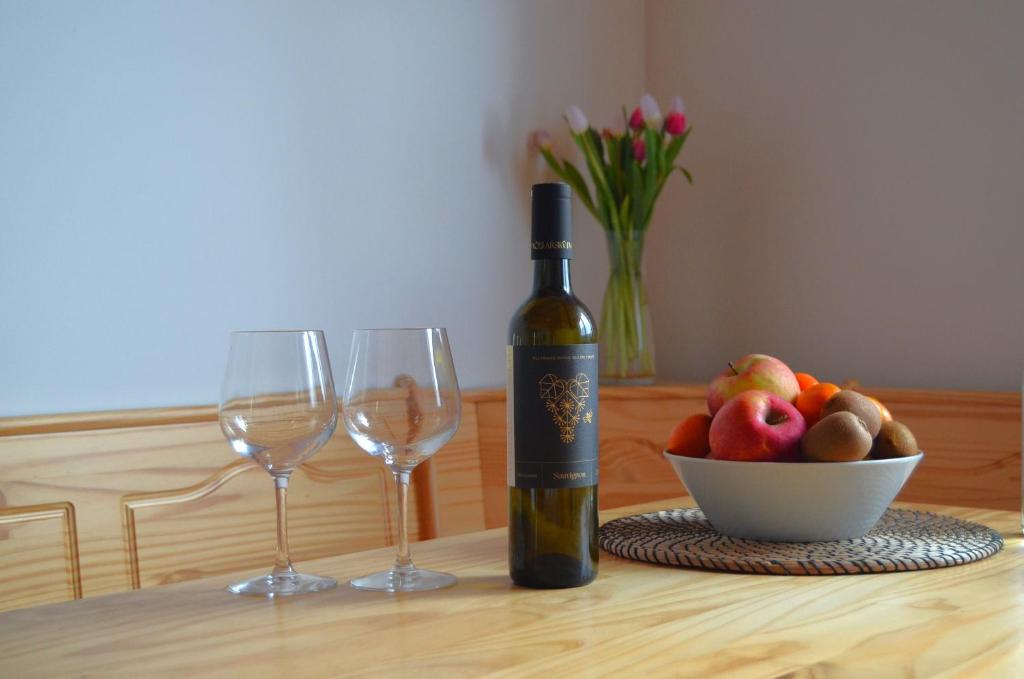 a bottle of wine next to two wine glasses and a bowl of fruit at Apartmány Réví in Hlohovec