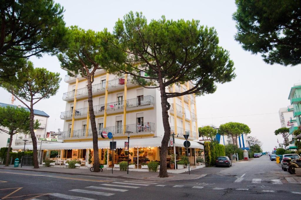 um edifício branco alto numa rua da cidade com árvores em Hotel Roma em Lido di Jesolo