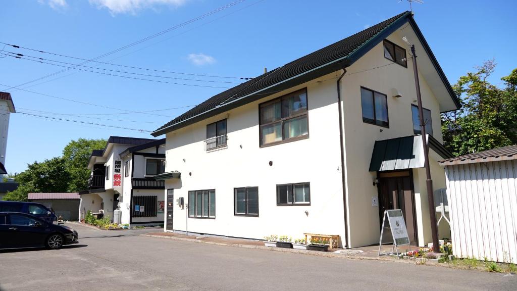 une maison blanche avec une voiture garée devant elle dans l'établissement Kawayu Onsen Guesthouse NOMY, à Kawayu