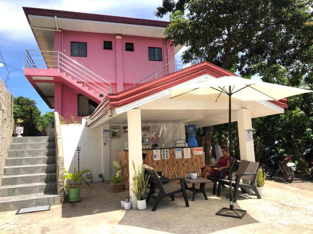 uma mulher sentada debaixo de um guarda-chuva em frente a um edifício cor-de-rosa em Chaniva-Joy Island View Appartments em Malapascua