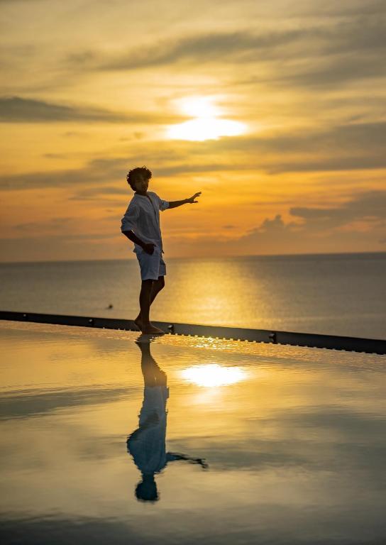 a person standing on the beach with the sunset in the background at Norn Talay Surin Beach Phuket in Surin Beach