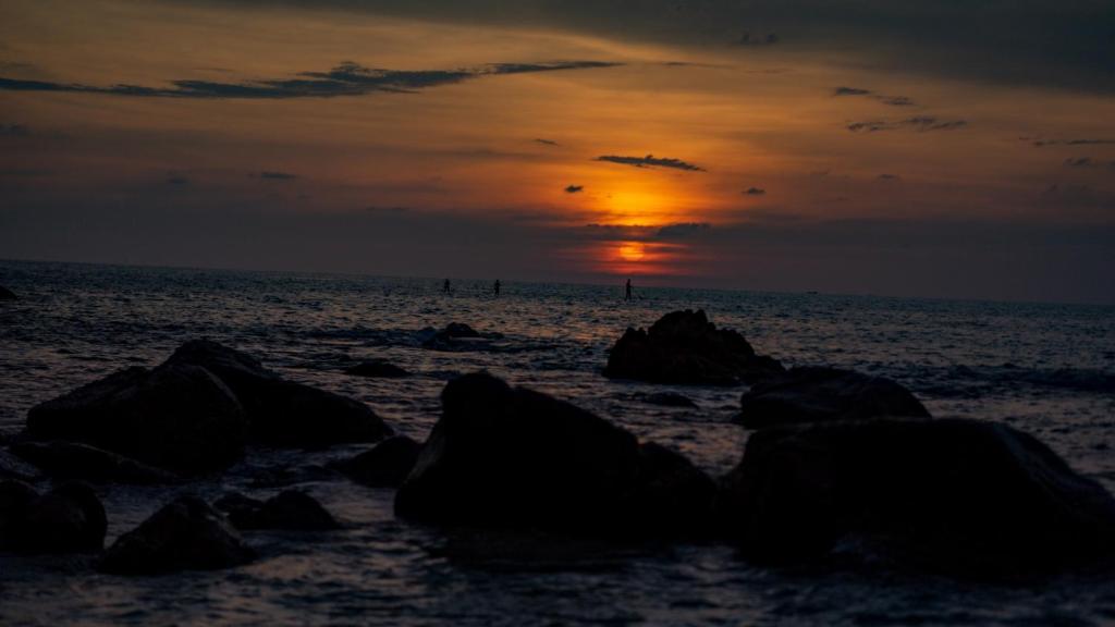 a sunset on the beach with rocks in the water at Norn Talay Surin Beach Phuket in Surin Beach