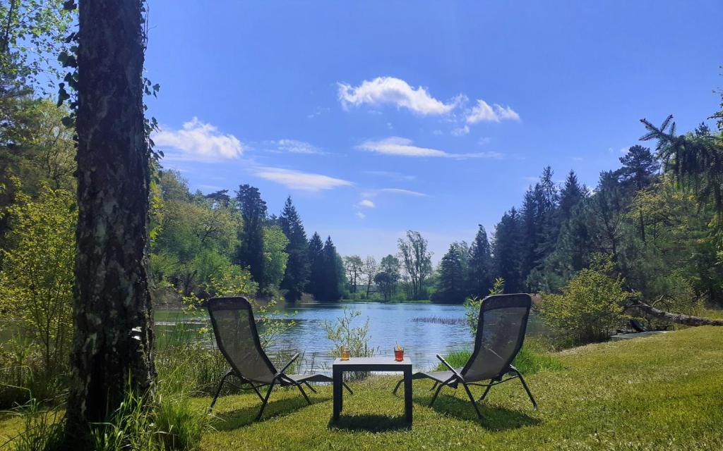 dos sillas y una mesa frente a un lago en Gîte nature détente pêche baignade dans lac privé, en Saint-Martin-des-Combes