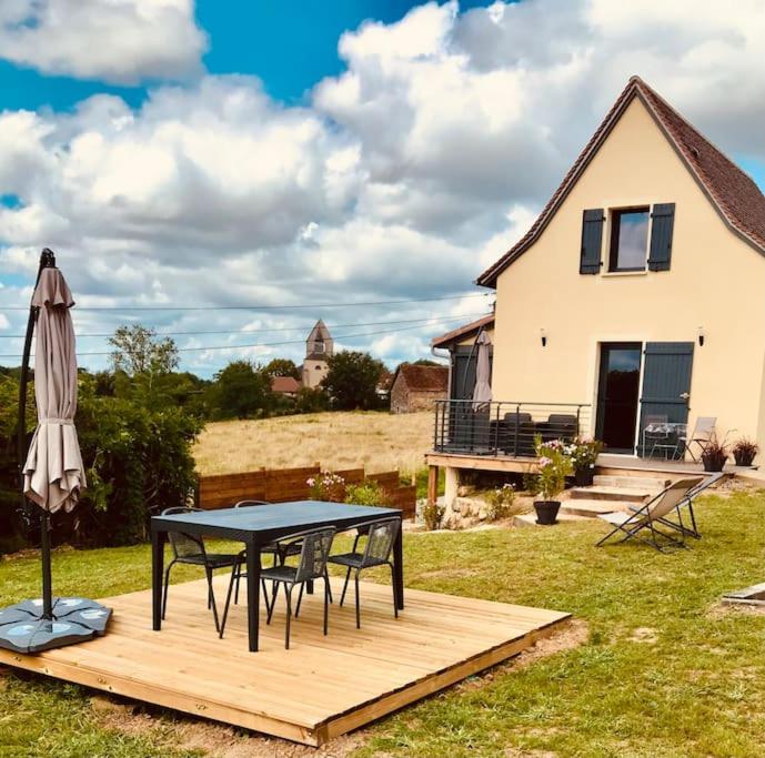 einen Tisch und einen Regenschirm auf einer Holzterrasse mit einem Haus in der Unterkunft Villa La Baronne-Hauteurs de Beaulieu-sur-Dordogne in Beaulieu-sur-Dordogne