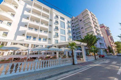 a white building with tables and umbrellas on a city street at Esal Hotel in Durrës