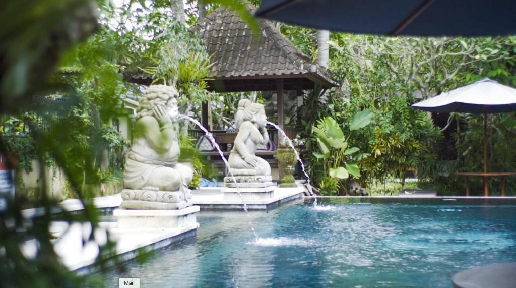 a swimming pool with two statues in a garden at Ubud Aura Retreat in Ubud