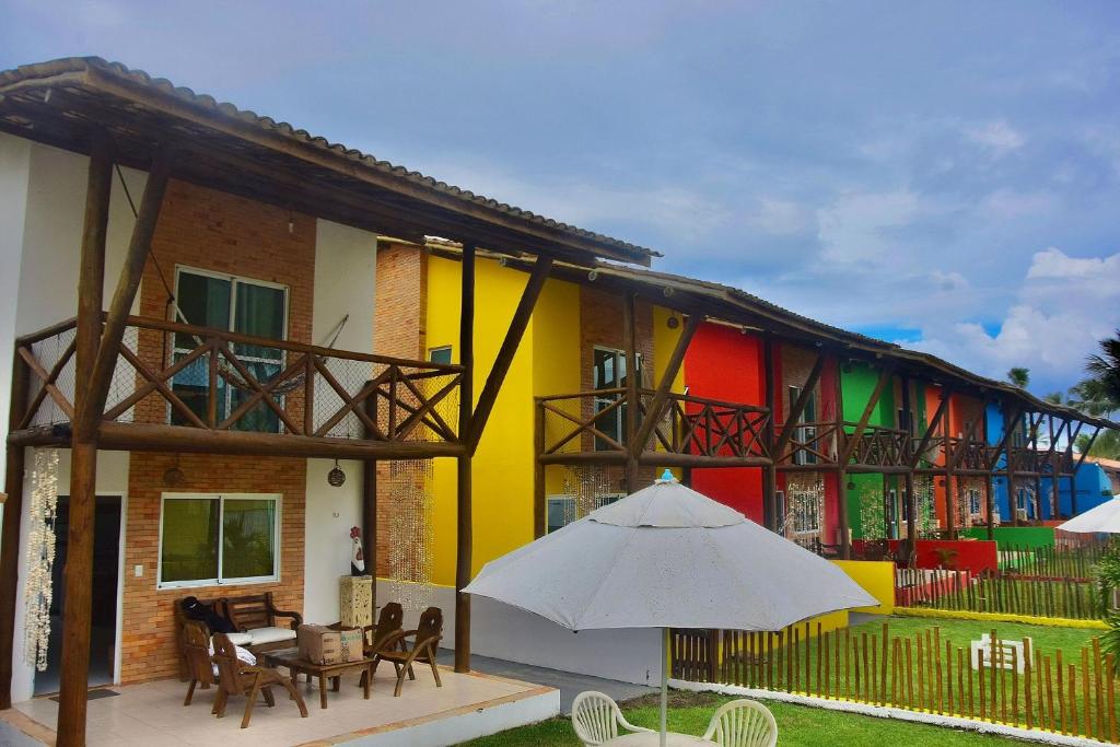 um edifício colorido com um guarda-chuva em frente em Vila Catuaí - 06 charmosos chalés há menos de 100m da Praia de Maracaípe em Porto de Galinhas