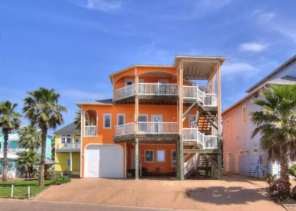 a large orange house with balconies and palm trees at 7 Bedroom Home STEPS TO THE BEACH With 4 Patios and Pool! Sleeps 20 in Port Aransas