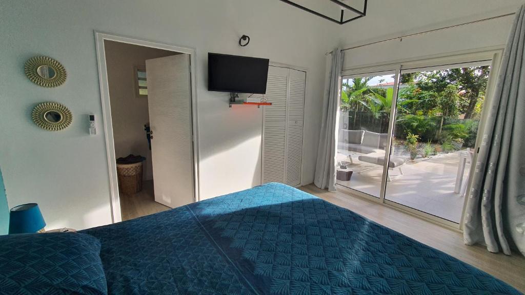 - une chambre avec un lit bleu et une porte coulissante en verre dans l'établissement LE MANGUIER, à Baie-Mahault