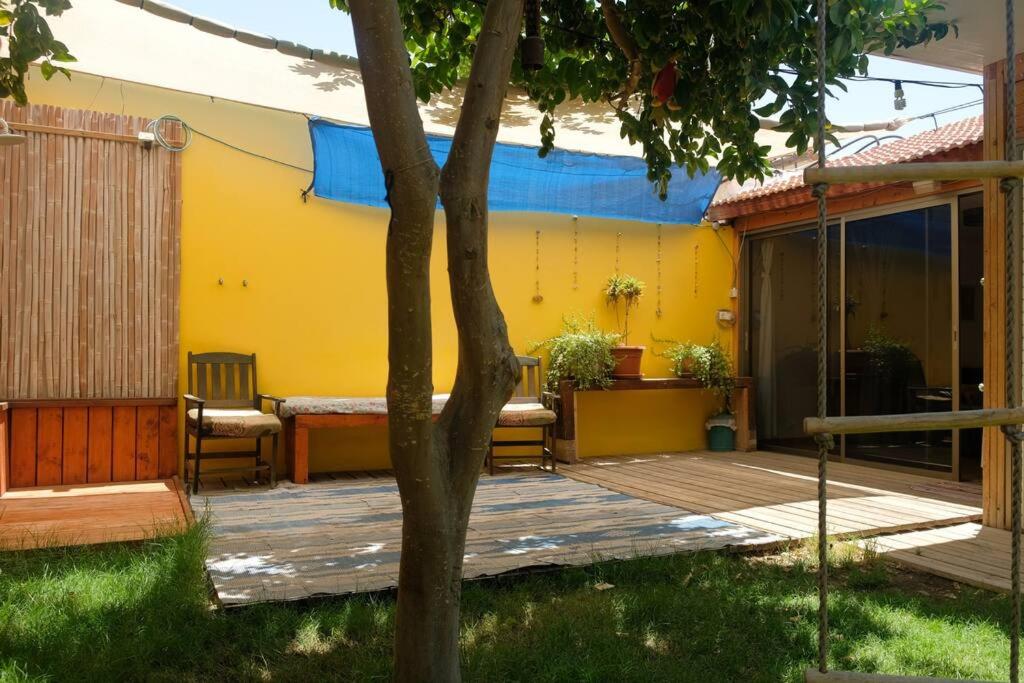 a wooden deck with chairs and a yellow house at Cosy Family Home & Garden in Eilat in Eilat