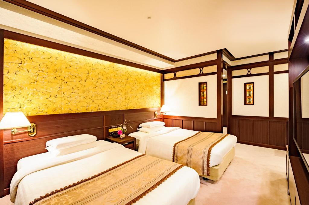 two beds in a hotel room with yellow wallpaper at Kanazawa Hakuchoro Hotel Sanraku -Natural Hot Spring- in Kanazawa