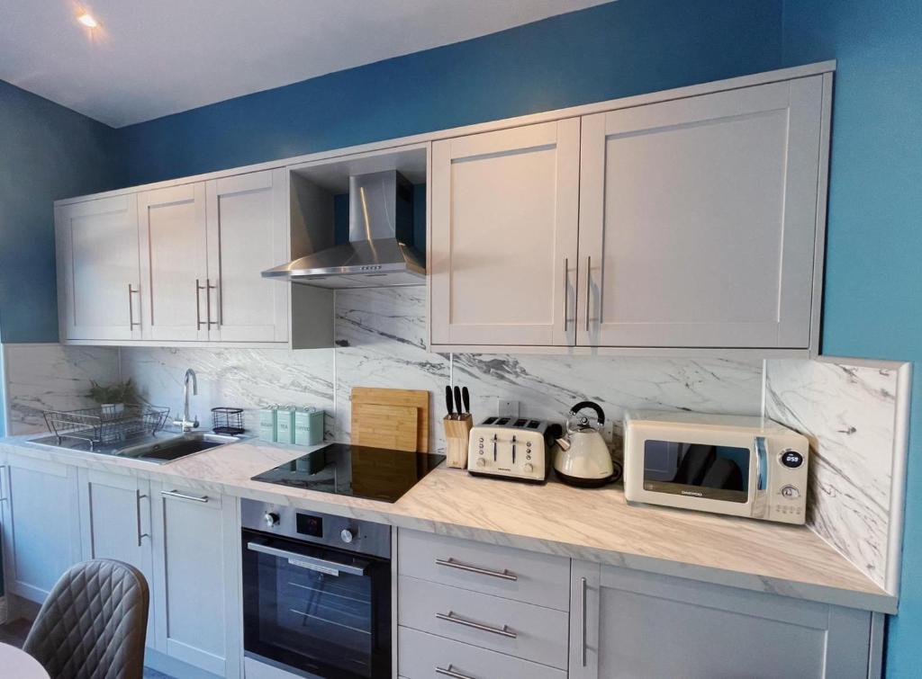 a kitchen with white cabinets and a microwave at Pier Plain By The Sea in Gorleston-on-Sea