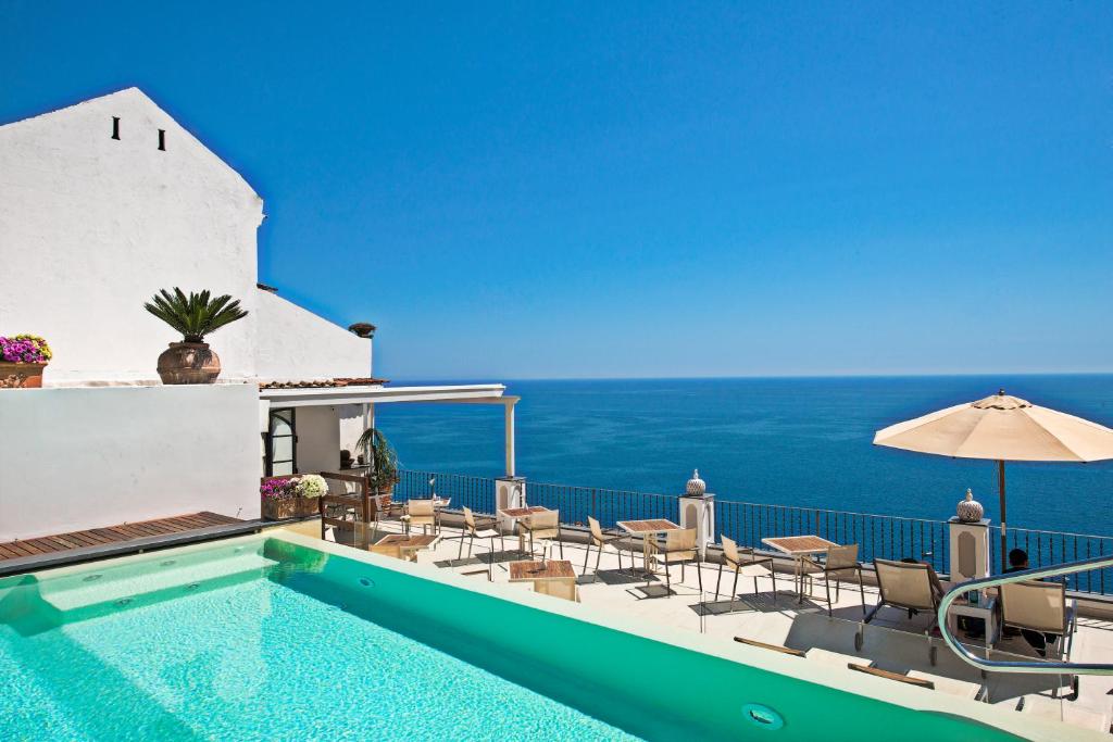 a swimming pool with chairs and an umbrella and the ocean at Hotel Punta Regina in Positano