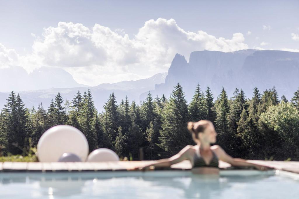 a woman in a swimming pool with mountains in the background at Hotel Tann in Collalbo