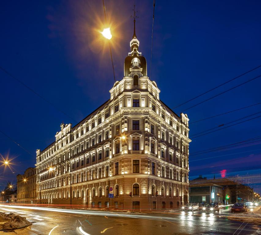 un grand bâtiment blanc avec une tour d'horloge la nuit dans l'établissement Aparthotel Amella, à Riga