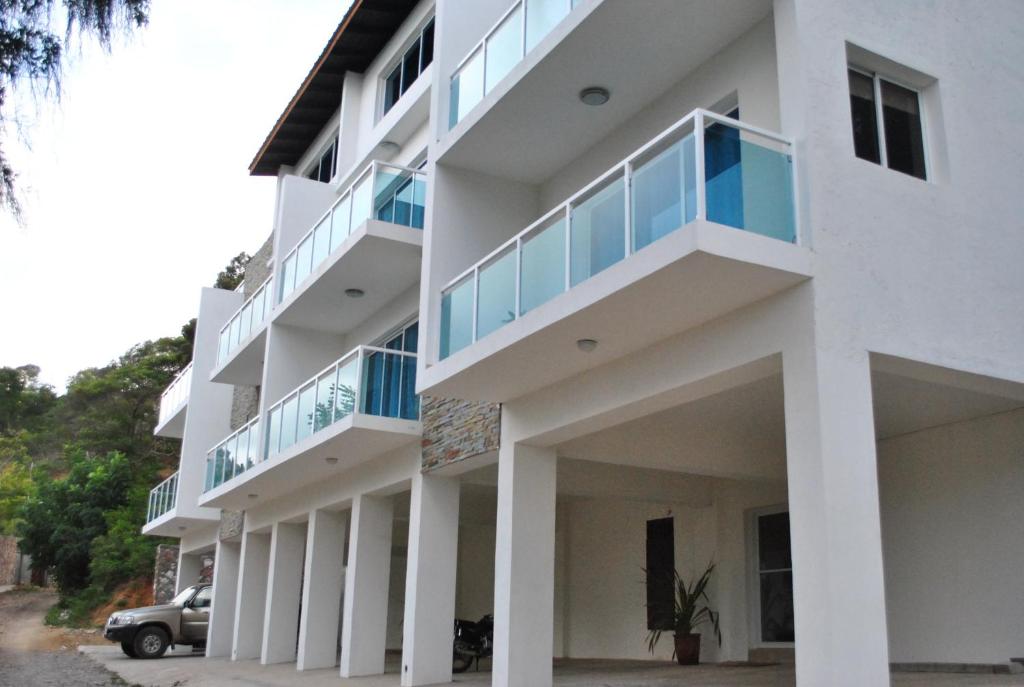 un edificio blanco con balcones y un coche aparcado delante en Vue Apartment Hotel, en Cabo Haitiano