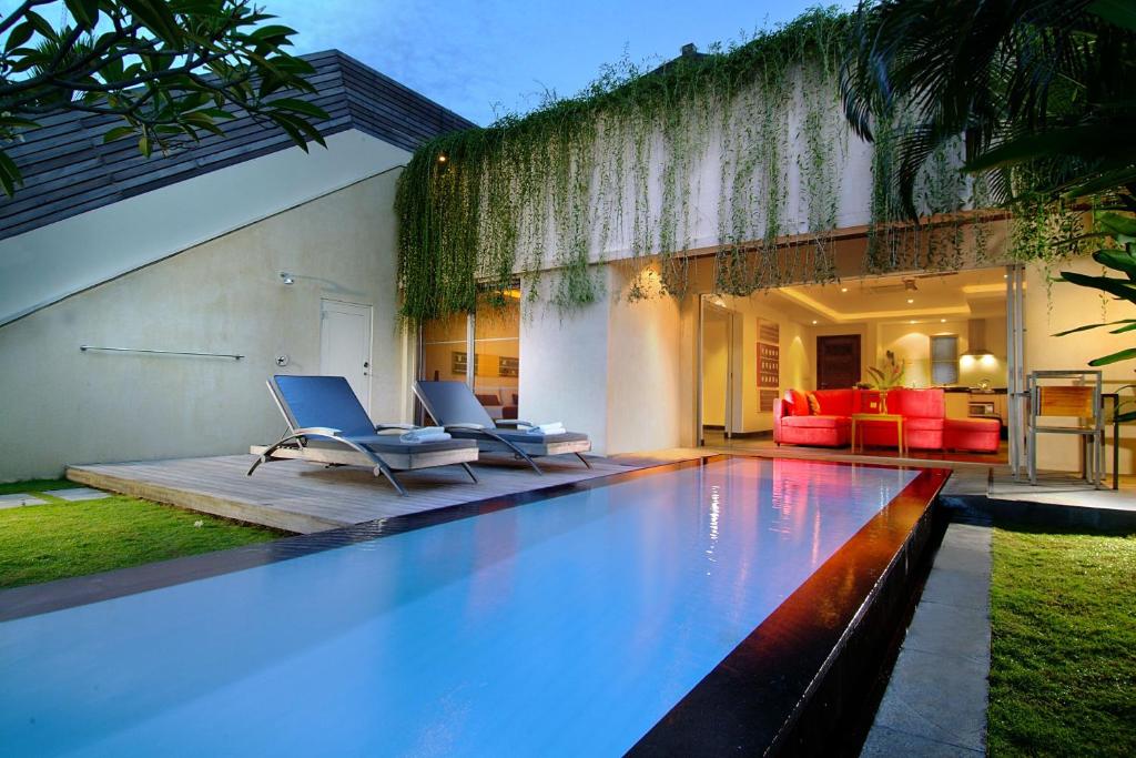 a swimming pool with two chairs and a house at Bali Island Villas & Spa CHSE Certified in Seminyak