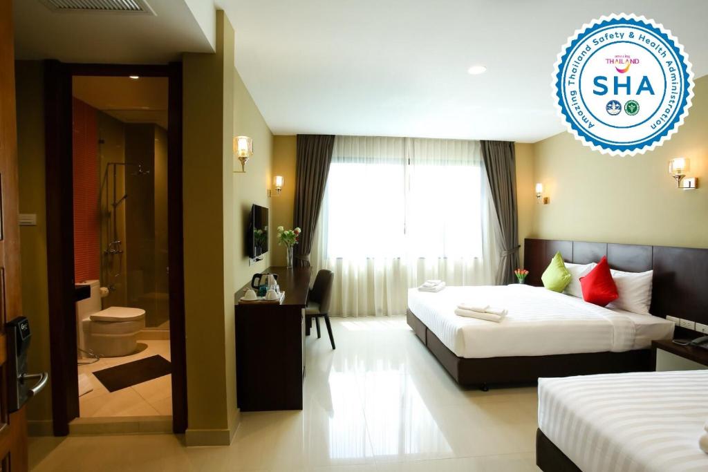 A bright twin room with a visible bathroom entrance, large window and two beds.