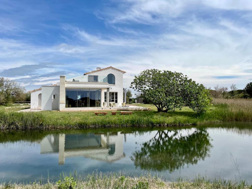 Mas du Couvin, maison d'hôtes en Camargue في سانت ماري دو لا مير: بيت ابيض وامامه بركه