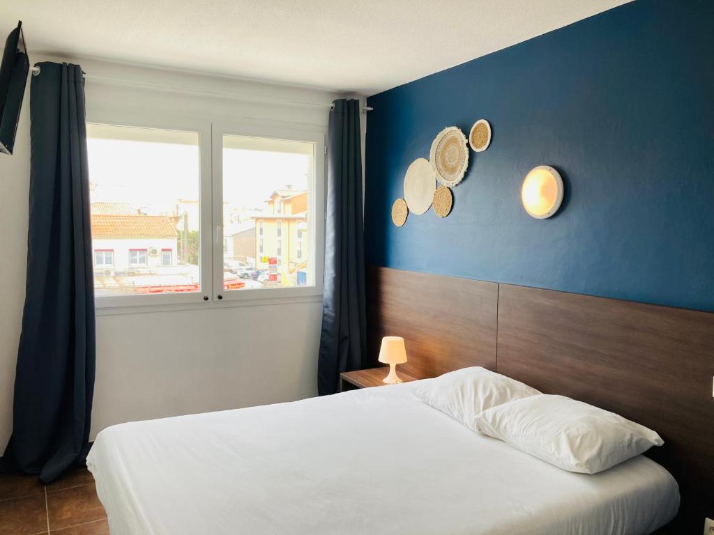 Cet appartement comprend une chambre dotée d'un lit avec un mur bleu et une fenêtre. dans l'établissement Hotel le Provençal, à Narbonne-Plage