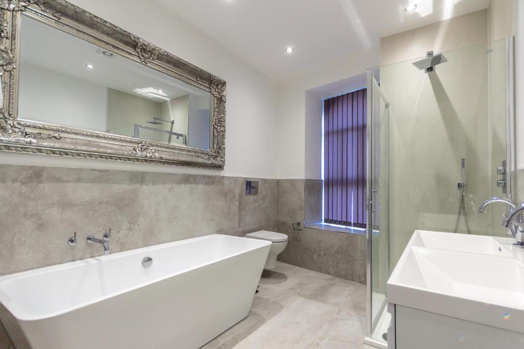 bagno con vasca, lavandino e specchio di The Regency Suite a Plymouth