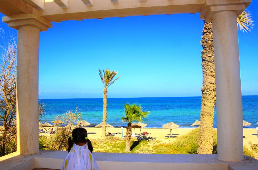 una niñita con un vestido blanco mirando hacia el océano en Zita Beach Resort, en Zarzis