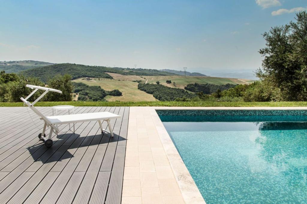 een witte stoel op een houten terras naast een zwembad bij Villa Chiugi by PosarelliVillas in Seggiano
