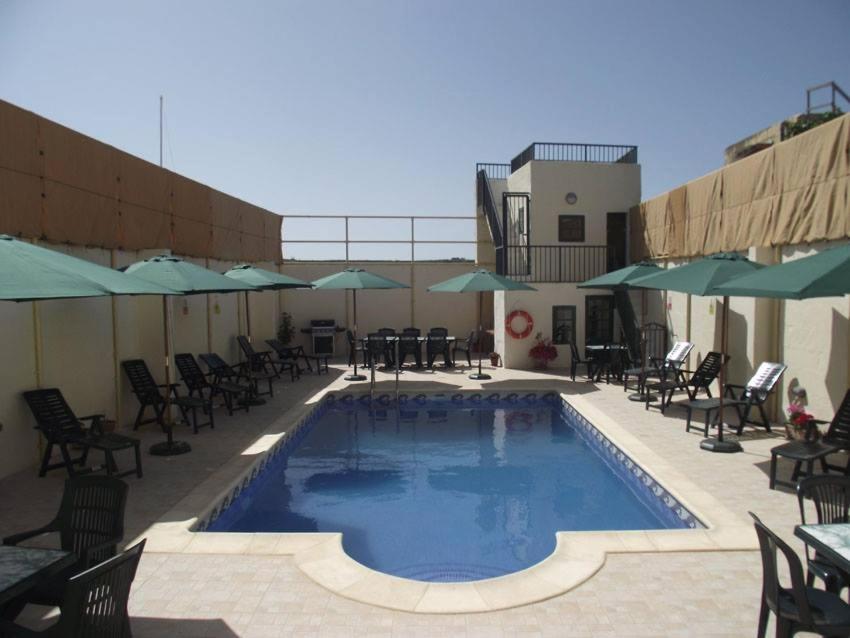 a swimming pool with chairs and tables and umbrellas at Qronfli Holiday Apartments With Swimming Pool in San Lawrenz
