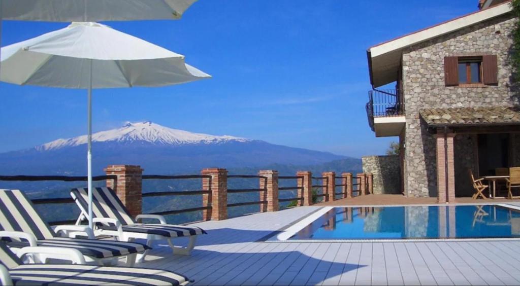 een zwembad met stoelen en een parasol en een berg bij Villa Etna Mare - Pool villa in peaceful location with breathtaking views of the sea, Mt Etna & Taormina - in Taormina