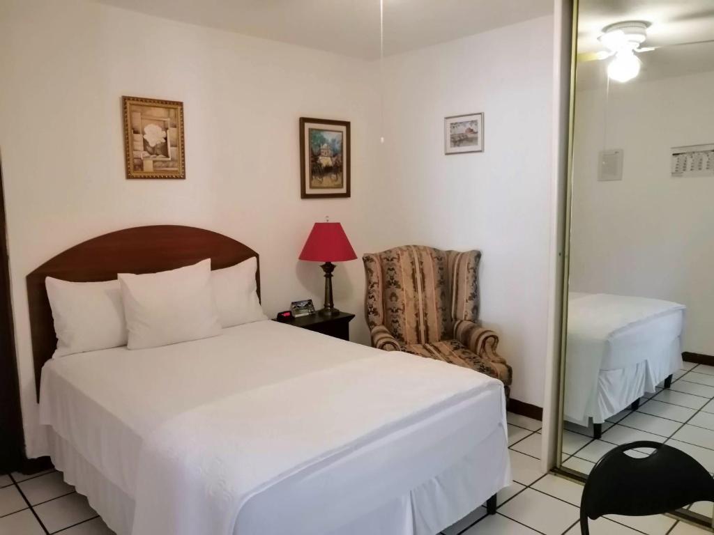 1 dormitorio con cama, espejo y silla en Novohostal B&B en Guatemala