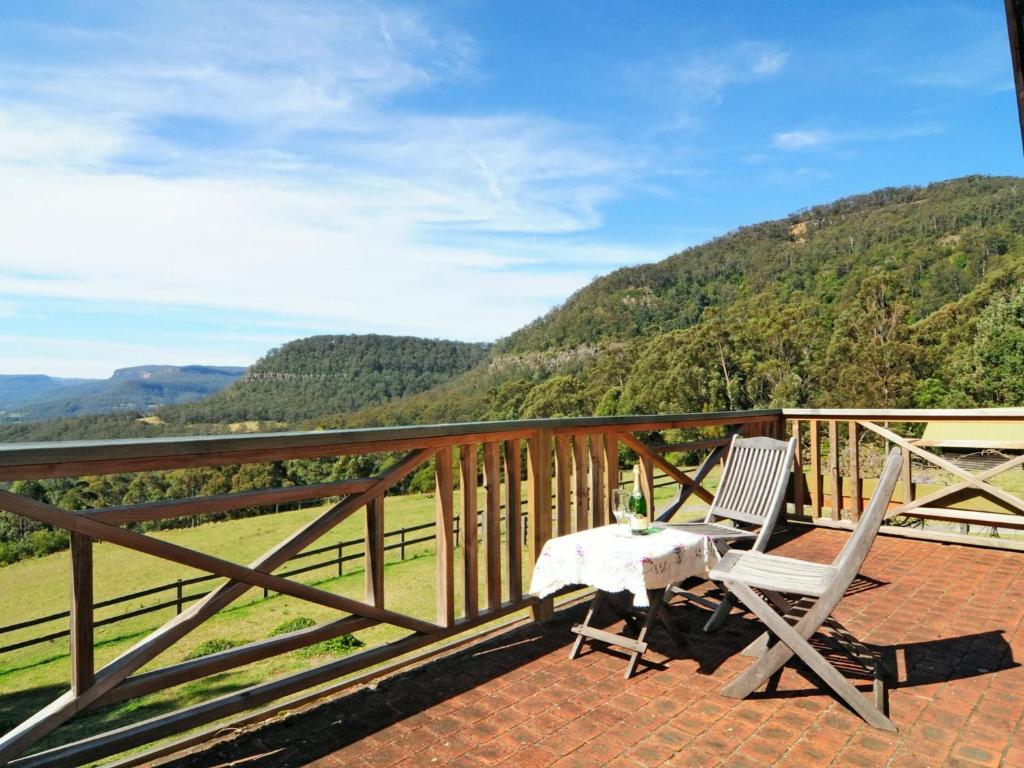 een tafel en 2 stoelen op een balkon met uitzicht op de bergen bij Alcheringa Cottage Amazing Location with views in Kangaroo Valley