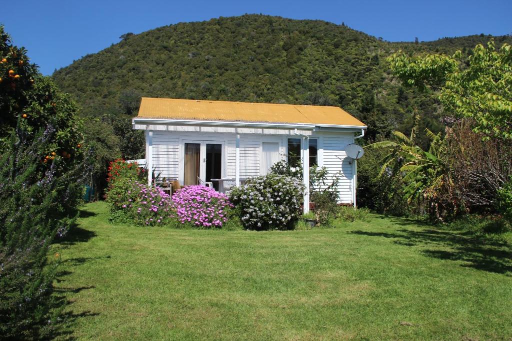 a small white house in a yard with flowers at Cottage - Whanarua Bay Cottages in Te Kaha