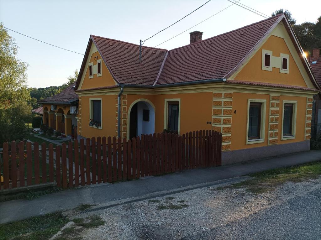 a small yellow house with a wooden fence at Nádkunyhó Vendégház in Hegyhátszentjakab