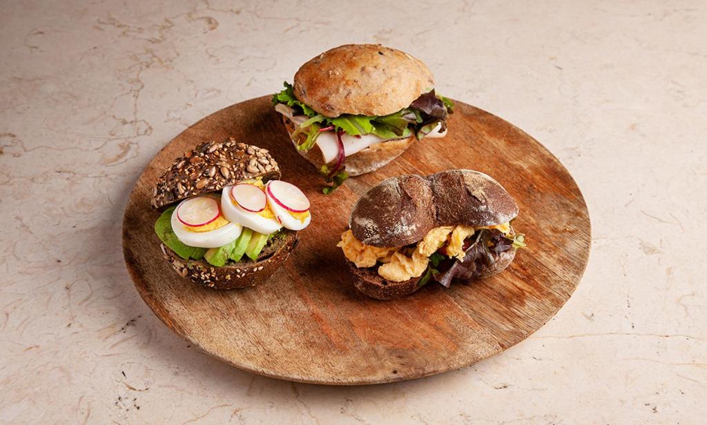 three sandwiches on a wooden plate on a table at RM The Experience - Small Portuguese Hotels in Setúbal