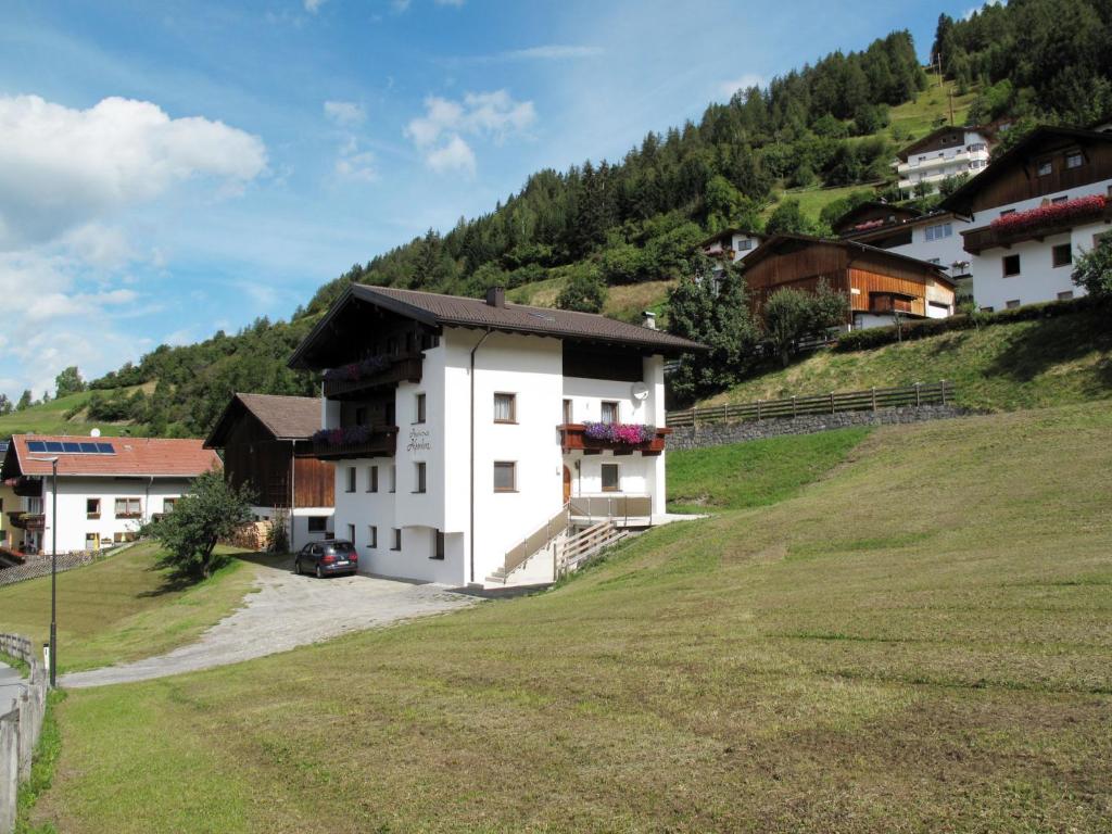 a white building on a grassy hill with houses at Apartment Alpenherz - PTZ431 by Interhome in Fendels