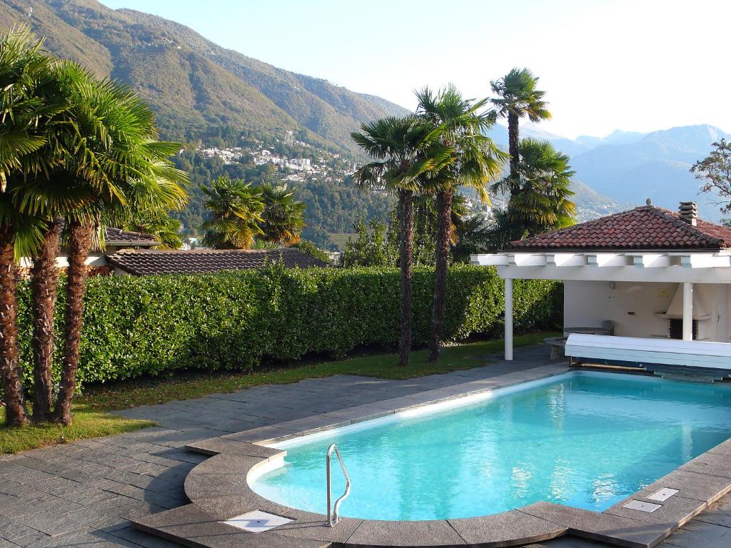 a swimming pool with palm trees and a house at Apartment Collina Verde B by Interhome in Ascona