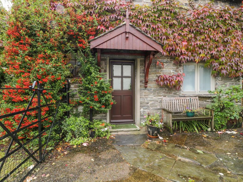 uma casa com uma porta e um banco e flores em Holemire Barn em Cockermouth