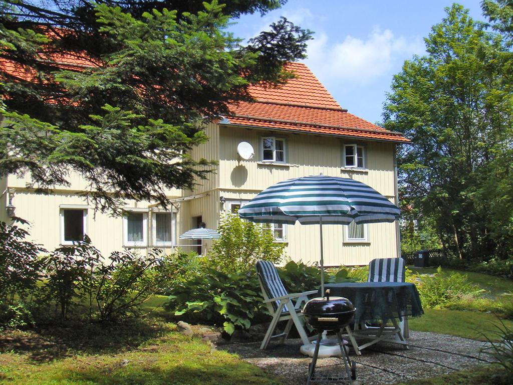 a house with a grill and two chairs and an umbrella at Apartment Altes Forsthaus Sösetal by Interhome in Riefensbeek