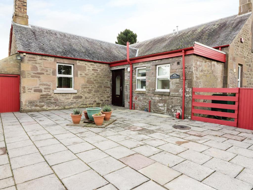 a brick house with a red fence and a patio at Meadowside Farm in Coupar Angus