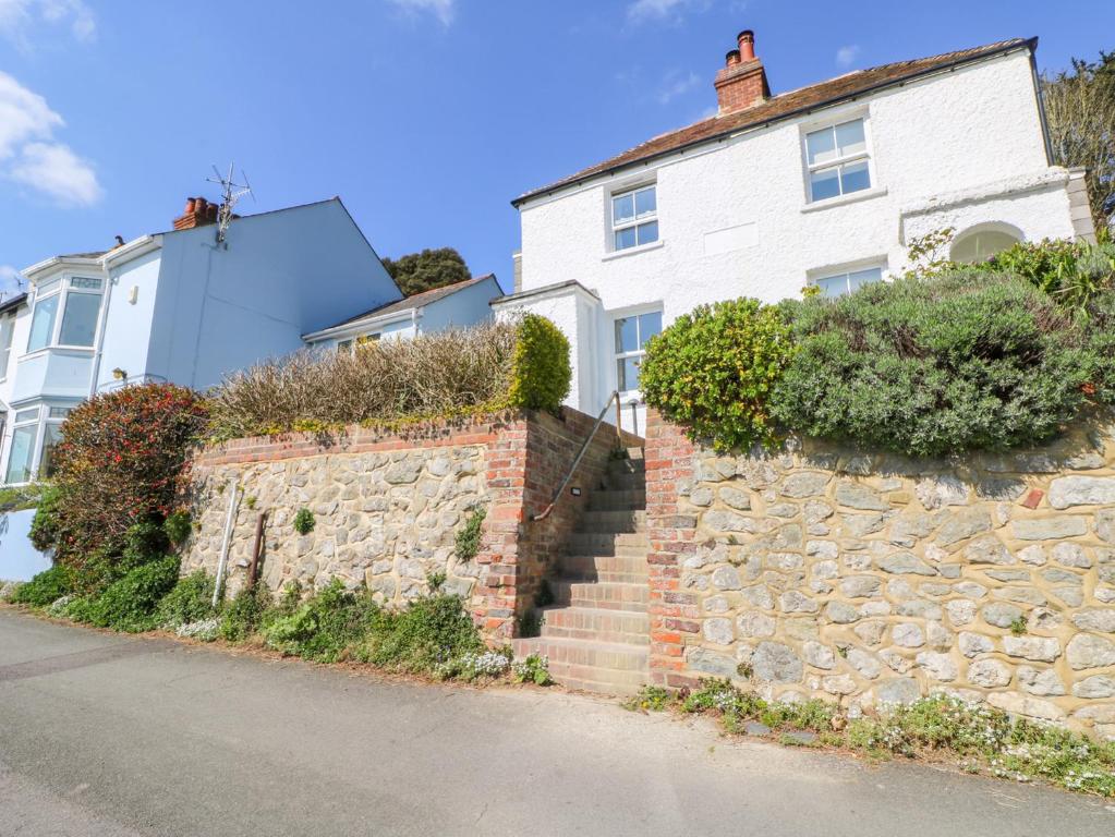 a white house with a stone wall and stairs at Kits Cottage in Hythe